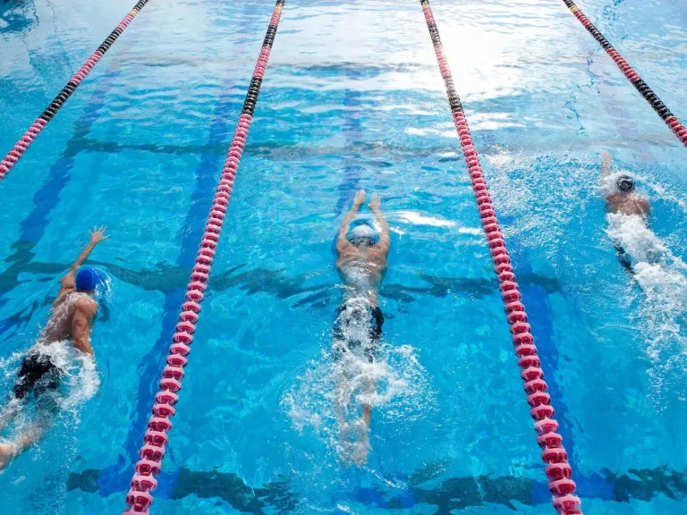 hree competitive swimmers race in separate lanes, with red lane lines contrasting against the aqua blue pool water.