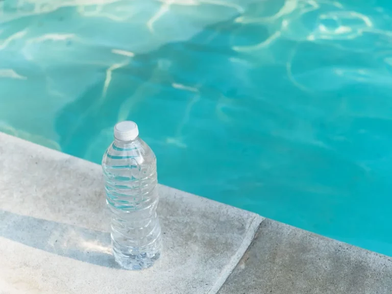 A close-up image of a clear water bottle placed on the grey cement poolside, with the aqua-colored swimming pool in the background. The page title, "The Essential Role of Hydration for Athletes and Competitive Swimmers," emphasizes the importance of athlete hydration.